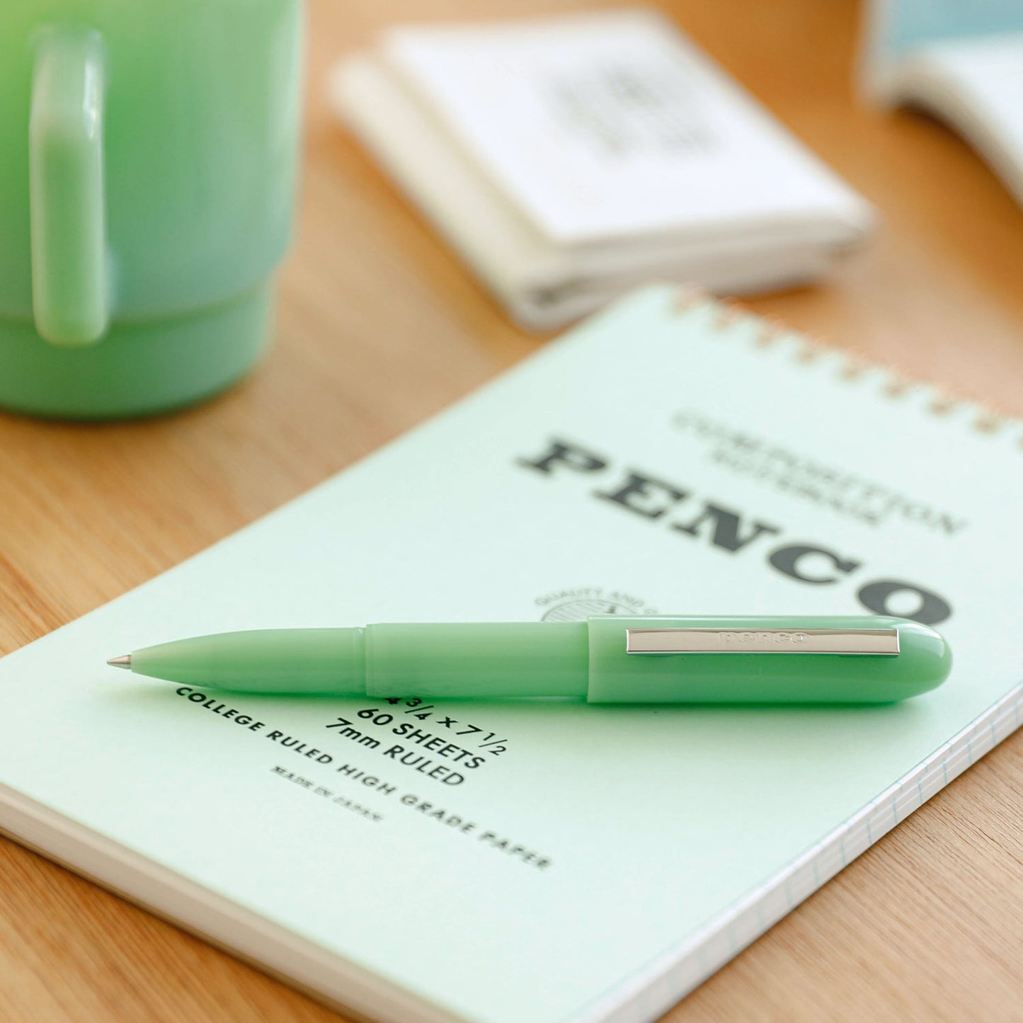 bullet pen with notebook in a table with green mint coffe cup and a blured image of a documents